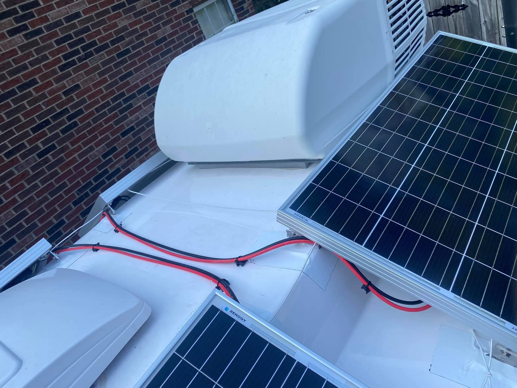 Solar-panel wiring and safety tethers routed around the rooftop air conditioner